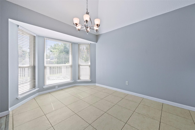 empty room featuring a chandelier, vaulted ceiling, light tile patterned floors, and baseboards