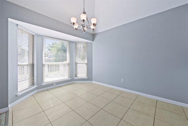empty room featuring a chandelier, vaulted ceiling, light tile patterned floors, and baseboards