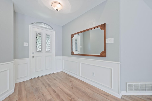 entrance foyer with wainscoting, light wood-style flooring, and a decorative wall