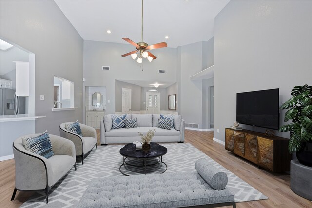 living room featuring ceiling fan, light wood finished floors, a high ceiling, baseboards, and recessed lighting