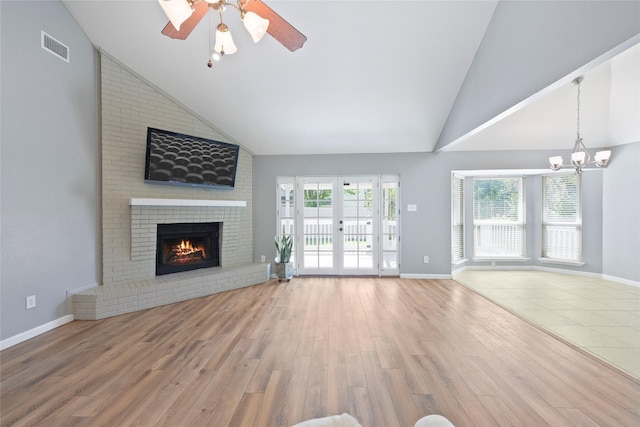 unfurnished living room with a fireplace, wood finished floors, a ceiling fan, a chandelier, and high vaulted ceiling