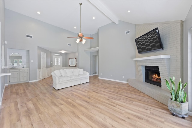 living room with high vaulted ceiling, light wood-style floors, a brick fireplace, a ceiling fan, and beam ceiling