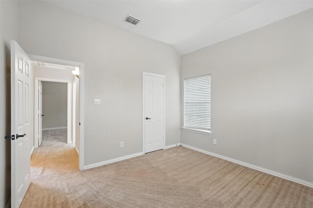 unfurnished bedroom featuring attic access, light carpet, vaulted ceiling, and baseboards