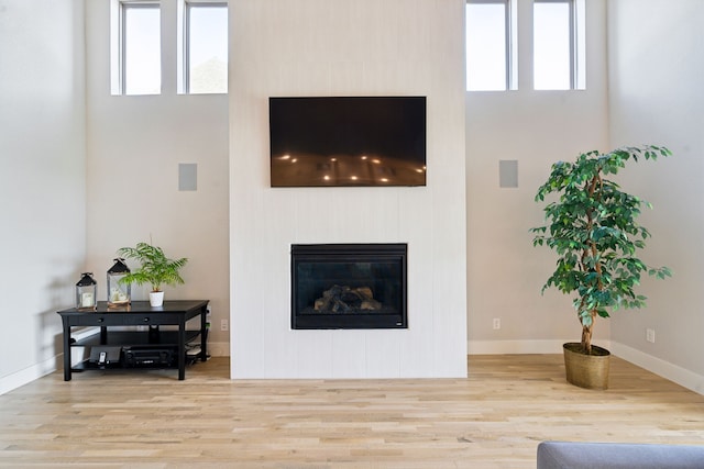 13417 Meadow Cross Dr, Fort Worth, TX 76008 - living area featuring wood finished floors, a glass covered fireplace, a high ceiling, healthy amount of natural light, and baseboards