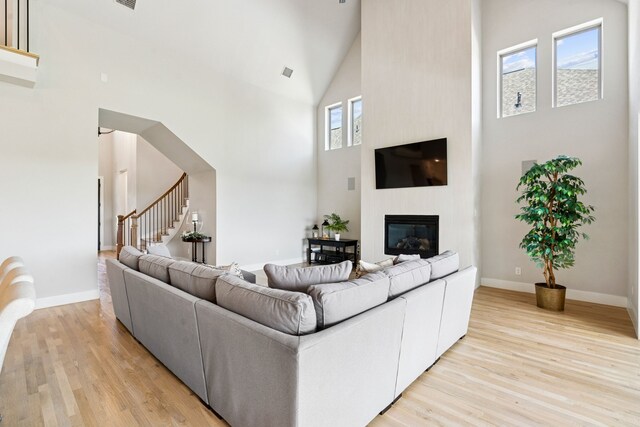 13417 Meadow Cross Dr, Fort Worth, TX 76008 - living area featuring high vaulted ceiling, light wood-style flooring, stairs, a glass covered fireplace, and baseboards