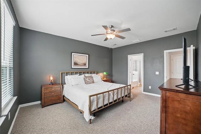 bedroom featuring light colored carpet, baseboards, ensuite bath, and a ceiling fan
