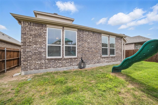 rear view of house featuring a playground and brick siding