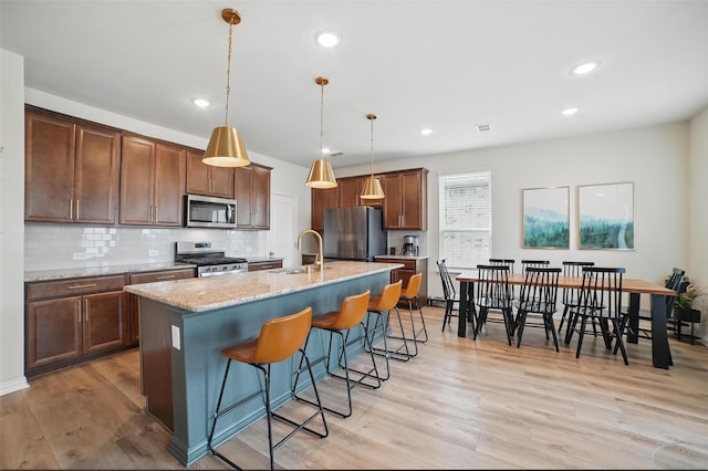 kitchen featuring appliances with stainless steel finishes, a sink, a kitchen breakfast bar, light wood-style flooring, and recessed lighting