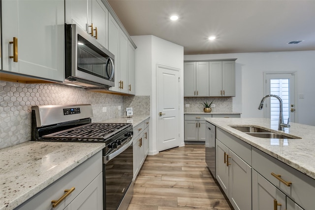 2665 Kings Canyon Mews, Corinth, TX 76210 - kitchen with appliances with stainless steel finishes, a sink, gray cabinetry, light wood-style flooring, and light stone counters