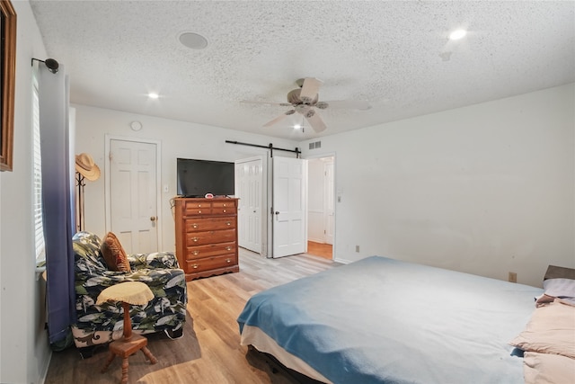 4548 Ivy Dr, Mesquite, TX 75150 - bedroom featuring a barn door, light wood finished floors, a textured ceiling, and ceiling fan