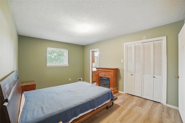 4548 Ivy Dr, Mesquite, TX 75150 - bedroom featuring light wood-type flooring, a textured ceiling, a glass covered fireplace, a closet, and baseboards