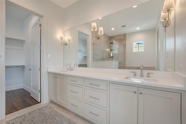 full bath featuring a shower stall, double vanity, wood finished floors, a walk in closet, and recessed lighting