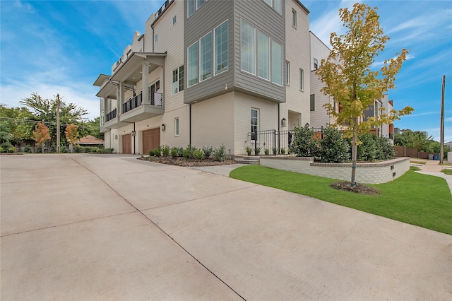 view of property exterior with an attached garage, driveway, a balcony, and a yard