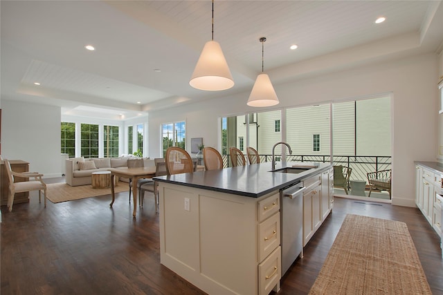 kitchen with a raised ceiling, a sink, stainless steel dishwasher, a kitchen island with sink, and dark wood-style floors
