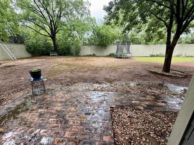 fenced backyard with a trampoline and a patio area