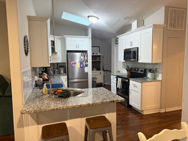 kitchen featuring appliances with stainless steel finishes, a peninsula, vaulted ceiling, backsplash, and dark wood-style floors