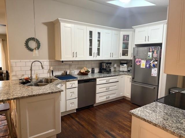kitchen featuring stainless steel appliances, a peninsula, a sink, and white cabinetry