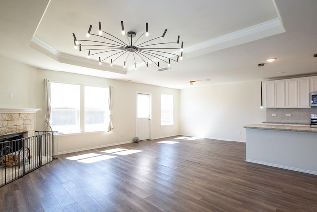 unfurnished living room featuring a tray ceiling, crown molding, dark wood finished floors, baseboards, and a fireplace