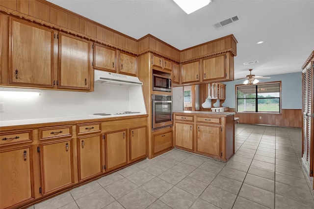 23010 County Road 3313, Chandler, TX 75758 - kitchen with stainless steel appliances, under cabinet range hood, a peninsula, brown cabinetry, and wainscoting