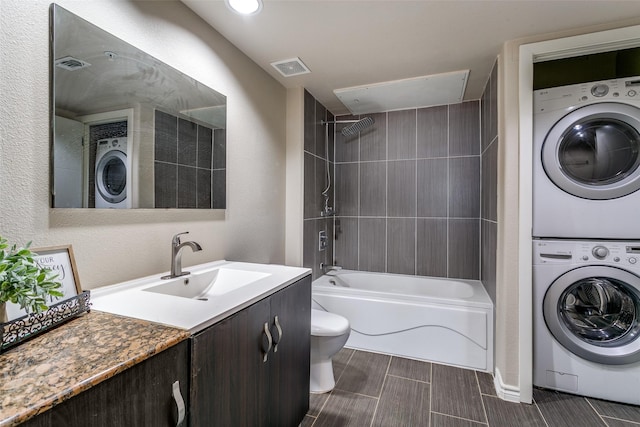 bathroom featuring stacked washer and clothes dryer, toilet, bathing tub / shower combination, and vanity