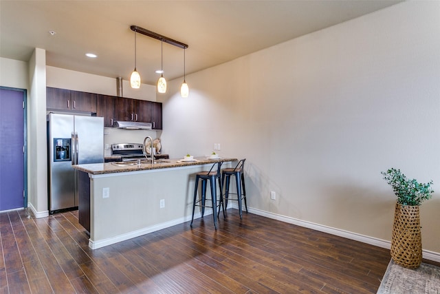 kitchen with stainless steel appliances, a sink, dark brown cabinetry, stone countertops, and a peninsula