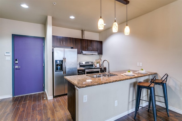 kitchen featuring stainless steel appliances, under cabinet range hood, a sink, a peninsula, and dark brown cabinetry