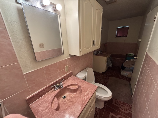 bathroom with tile walls, toilet, vanity, a wainscoted wall, and tile patterned flooring