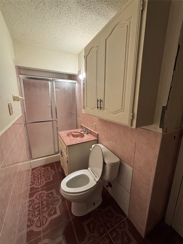 bathroom with tile walls, a textured ceiling, toilet, a shower stall, and tile patterned floors
