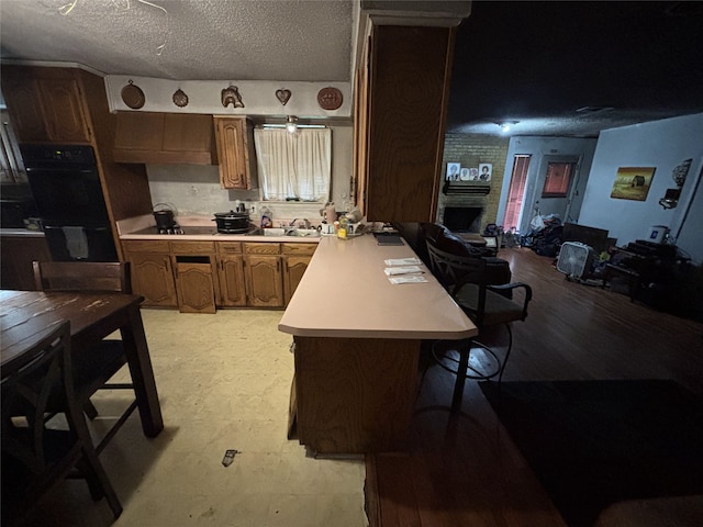 kitchen featuring light countertops, a peninsula, a sink, a kitchen bar, and brown cabinets