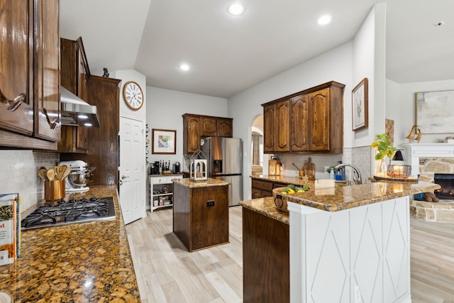 9529 Cholla Cactus Trl, Fort Worth, TX 76177 - kitchen with exhaust hood, stainless steel appliances, arched walkways, a stone fireplace, and a peninsula