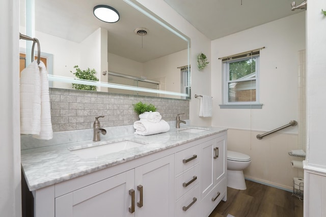 bathroom featuring toilet, wood finished floors, double vanity, backsplash, and a shower
