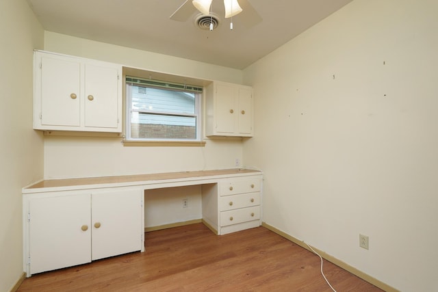 unfurnished office featuring built in study area, light wood-style flooring, ceiling fan, and baseboards
