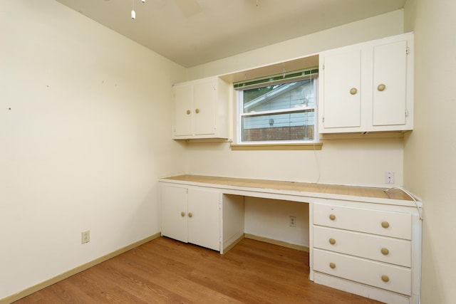 unfurnished office featuring light wood-style floors, built in desk, baseboards, and ceiling fan