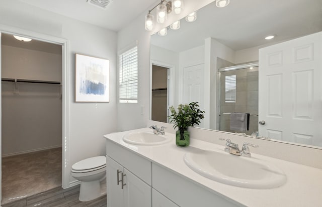 full bath featuring a stall shower, toilet, wood finished floors, double vanity, and a walk in closet