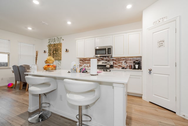 1034 Manuel Dr, Fate, TX 75087 - kitchen with stainless steel appliances, backsplash, light wood finished floors, a kitchen breakfast bar, and white cabinets