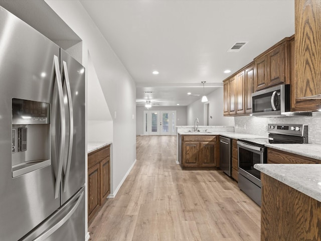 kitchen with appliances with stainless steel finishes, a sink, light wood finished floors, decorative backsplash, and light countertops