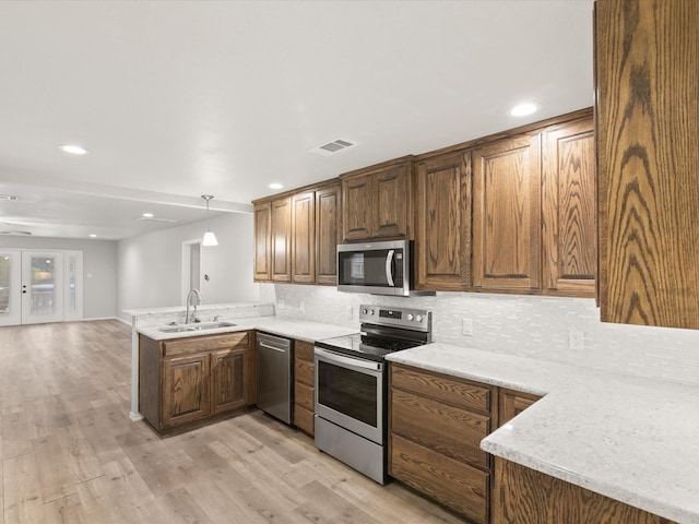 kitchen with appliances with stainless steel finishes, a sink, a peninsula, tasteful backsplash, and light wood-style floors