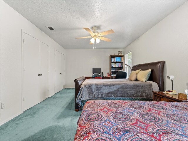 carpeted bedroom with a textured ceiling, a ceiling fan, and multiple closets