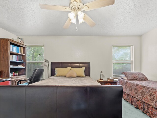 bedroom featuring a textured ceiling, multiple windows, a ceiling fan, an office area, and carpet floors