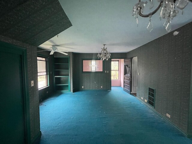 unfurnished living room with a chandelier, carpet, healthy amount of natural light, wallpapered walls, and a ceiling fan
