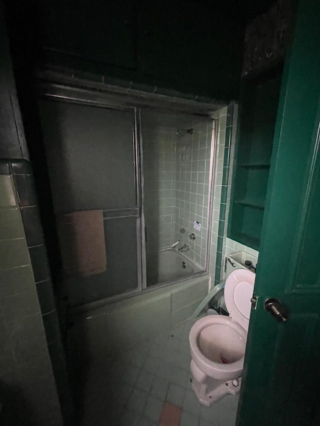 full bath with tile patterned floors, bath / shower combo with glass door, and toilet
