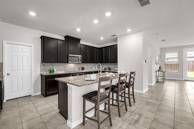 3433 Alamosa River Dr, Celina, TX 75078 - kitchen with stainless steel microwave, tasteful backsplash, light stone countertops, light tile patterned flooring, and a sink