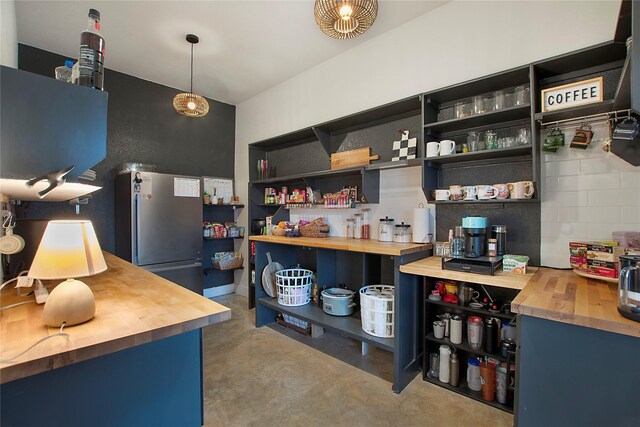 bar area with freestanding refrigerator, concrete flooring, and decorative light fixtures