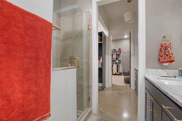bathroom featuring a stall shower, a walk in closet, finished concrete flooring, and vanity