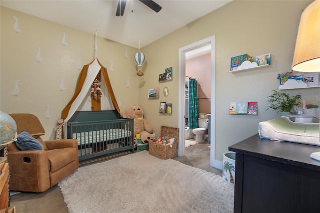 bedroom with concrete floors, a nursery area, ensuite bath, and ceiling fan