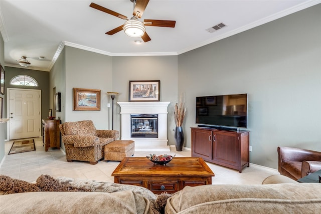 living room with light tile patterned flooring, ceiling fan, ornamental molding, a glass covered fireplace, and baseboards