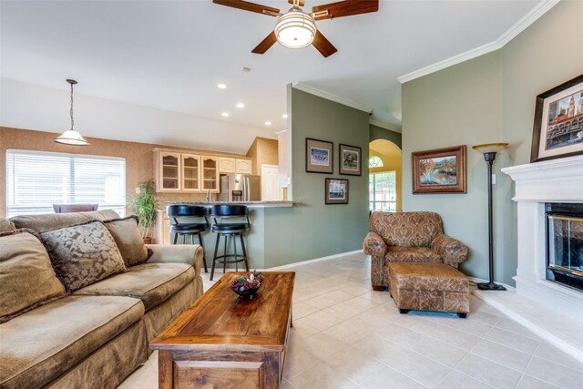 living room featuring a ceiling fan, arched walkways, crown molding, light tile patterned floors, and baseboards