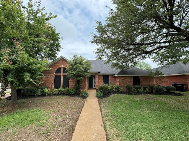view of front of house featuring a front yard, brick siding, and roof with shingles