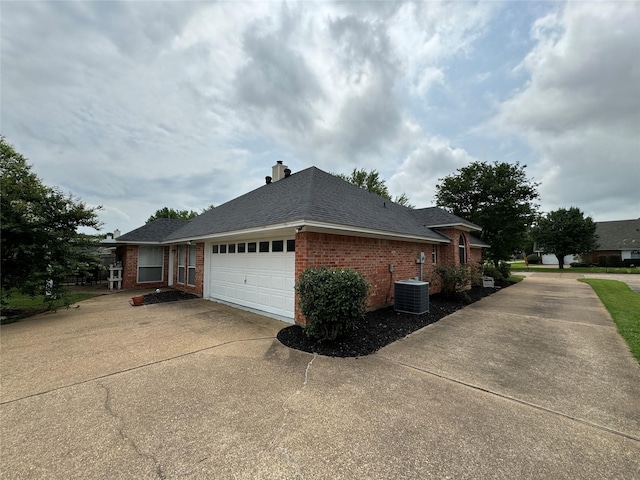 view of side of property featuring driveway, central AC, a garage, brick siding, and a chimney