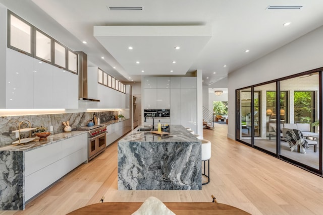 kitchen featuring modern cabinets, range with two ovens, wall chimney exhaust hood, white cabinets, and a sink